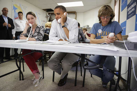 U.S. President Barack Obama (C) sits between campaign volunteers Alexa Kissinger (L) and Suzanne Stern as he makes calls to local volunteers to thank them for their work from a campaign office in Williamsburg, Virginia, October 14, 2012. REUTERS/Jonathan 