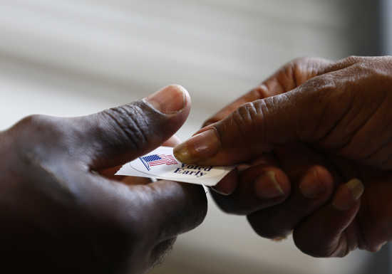 A poll worker hands a sticker to a voter at a polling place in Charlotte, North Carolina October 27, 2012. REUTERS/Chris Keane